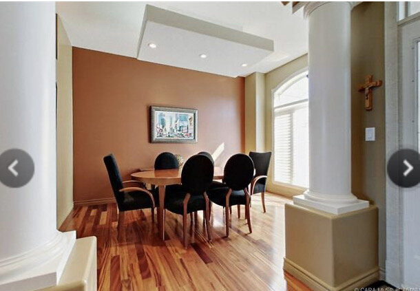 dining room with reddish brown walls, wood floors, arched opening flanked by large columns