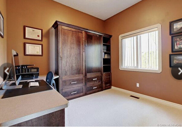 office with built in cabinets in brown dark shaker style wood and orange walls and one window