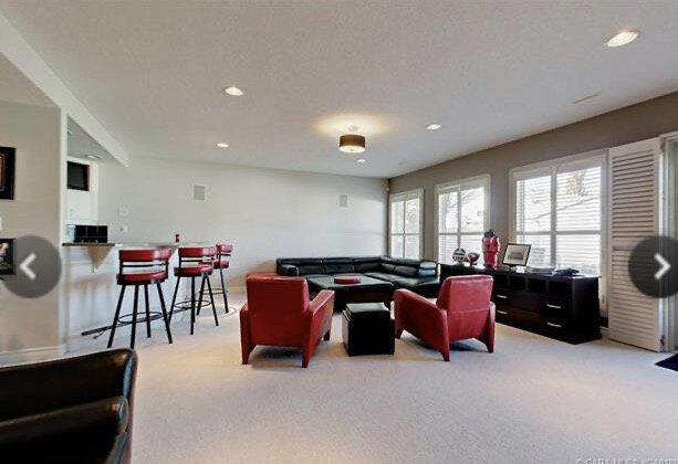 large room with raised bar on the left and beige walls and beige carpet, red and black leather furniture