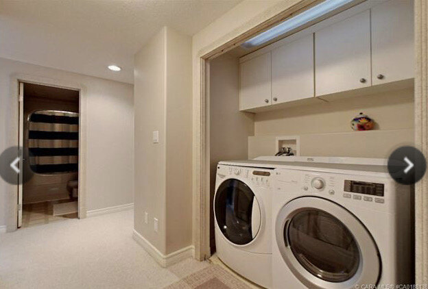 washer and dryer in a closet with no door in a beige painted hallway with bathoom in the background