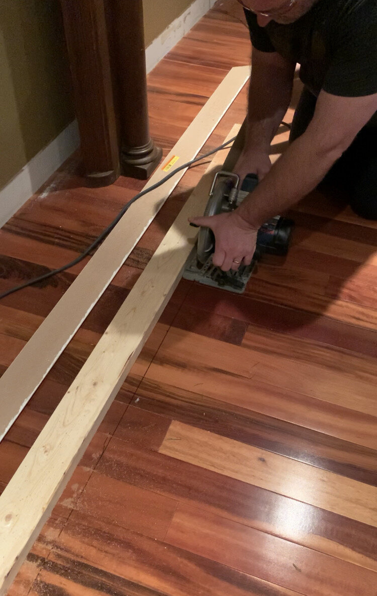 using a circular saw to cut hardwood out of the floor using a 2x4 nailed to the floor as a guide for a straight line
