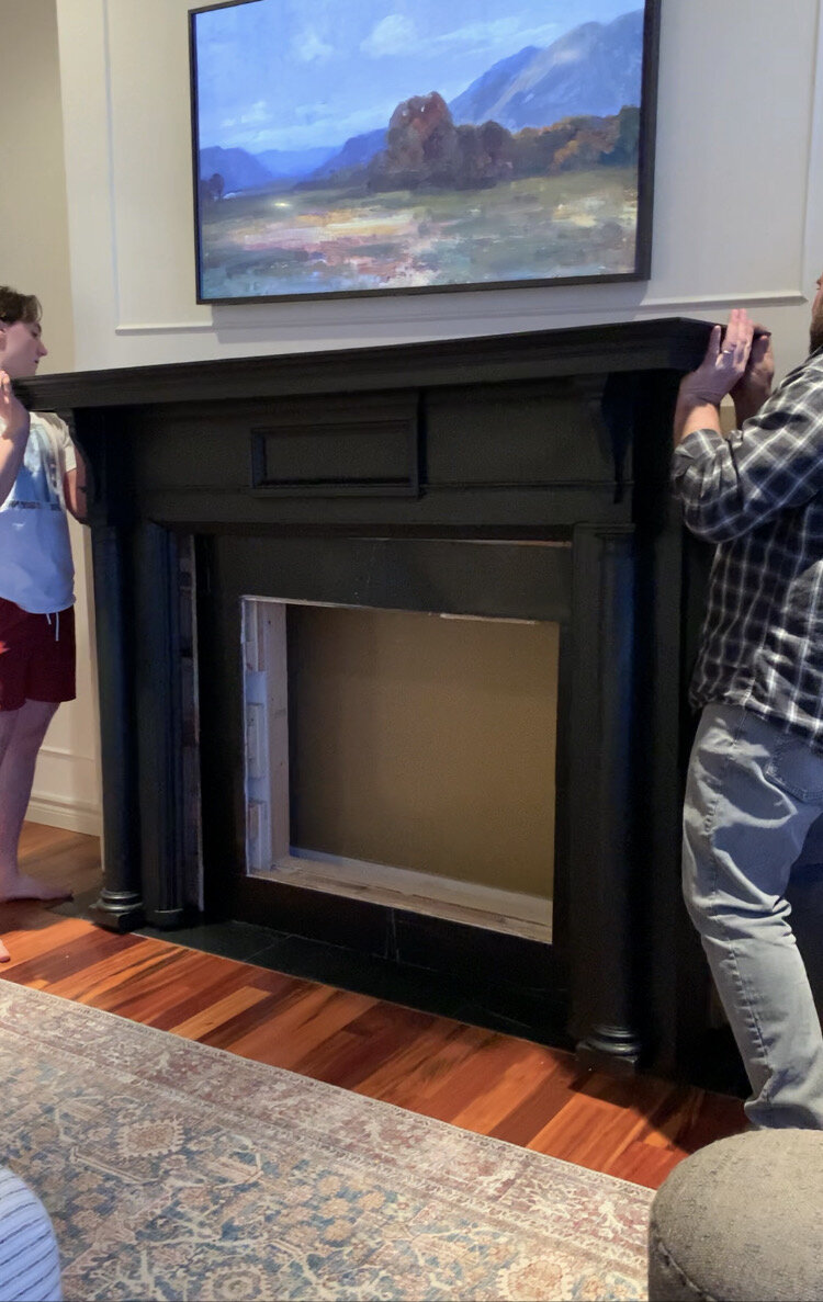 lifting the antique mantel in place overtop of the opening for the fireplace insert