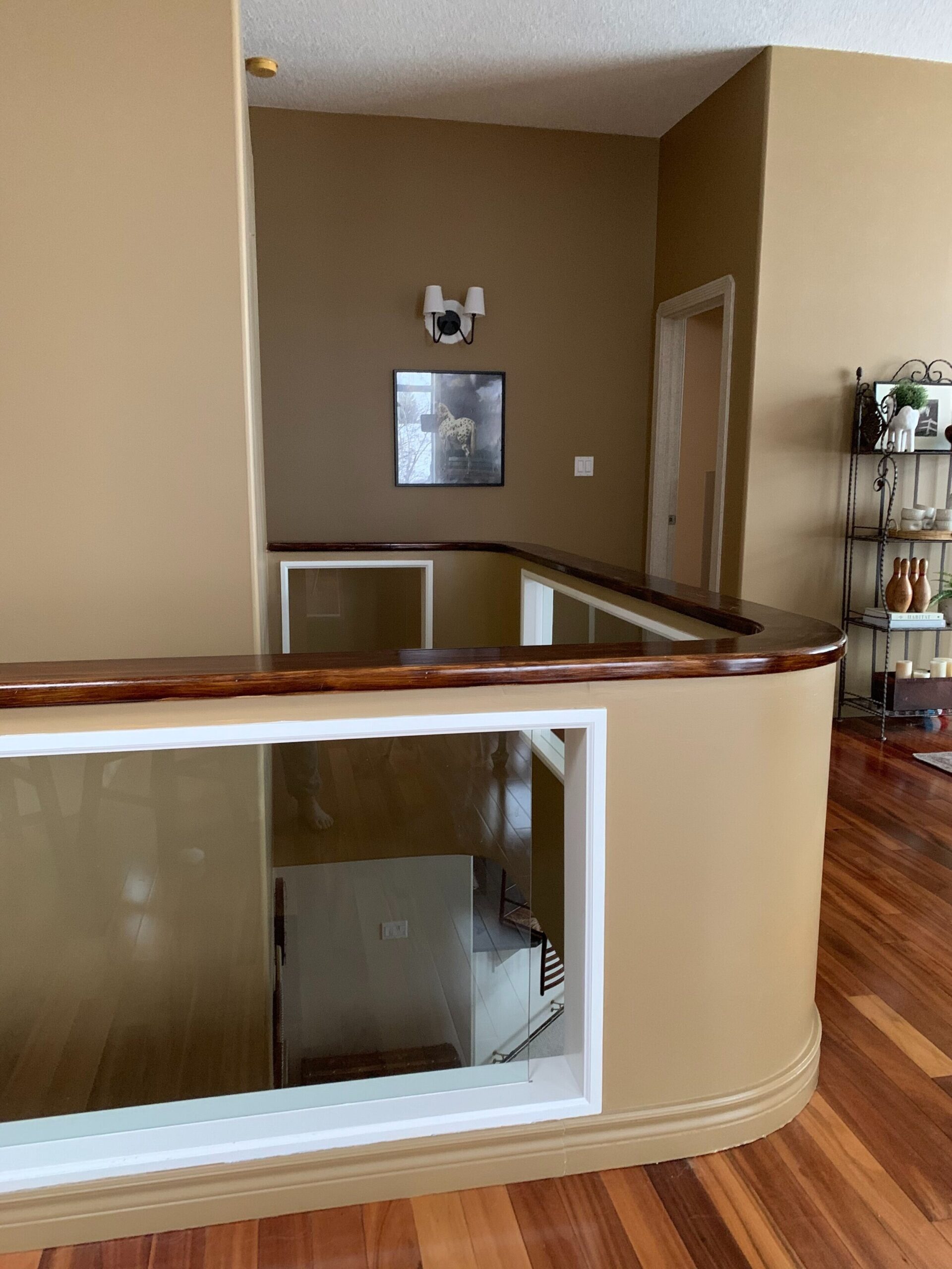 stairwel and hallway with a pony wall railing with glass insert and brown walls