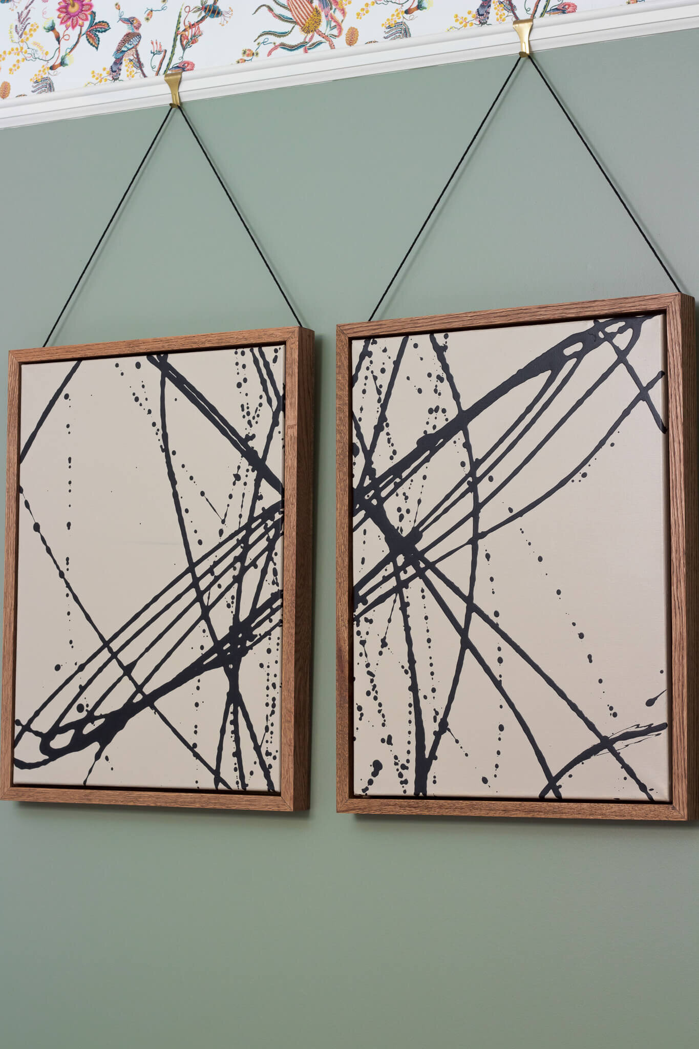 two abstract art pieces with oak frames hanging from a string from a picture rail
