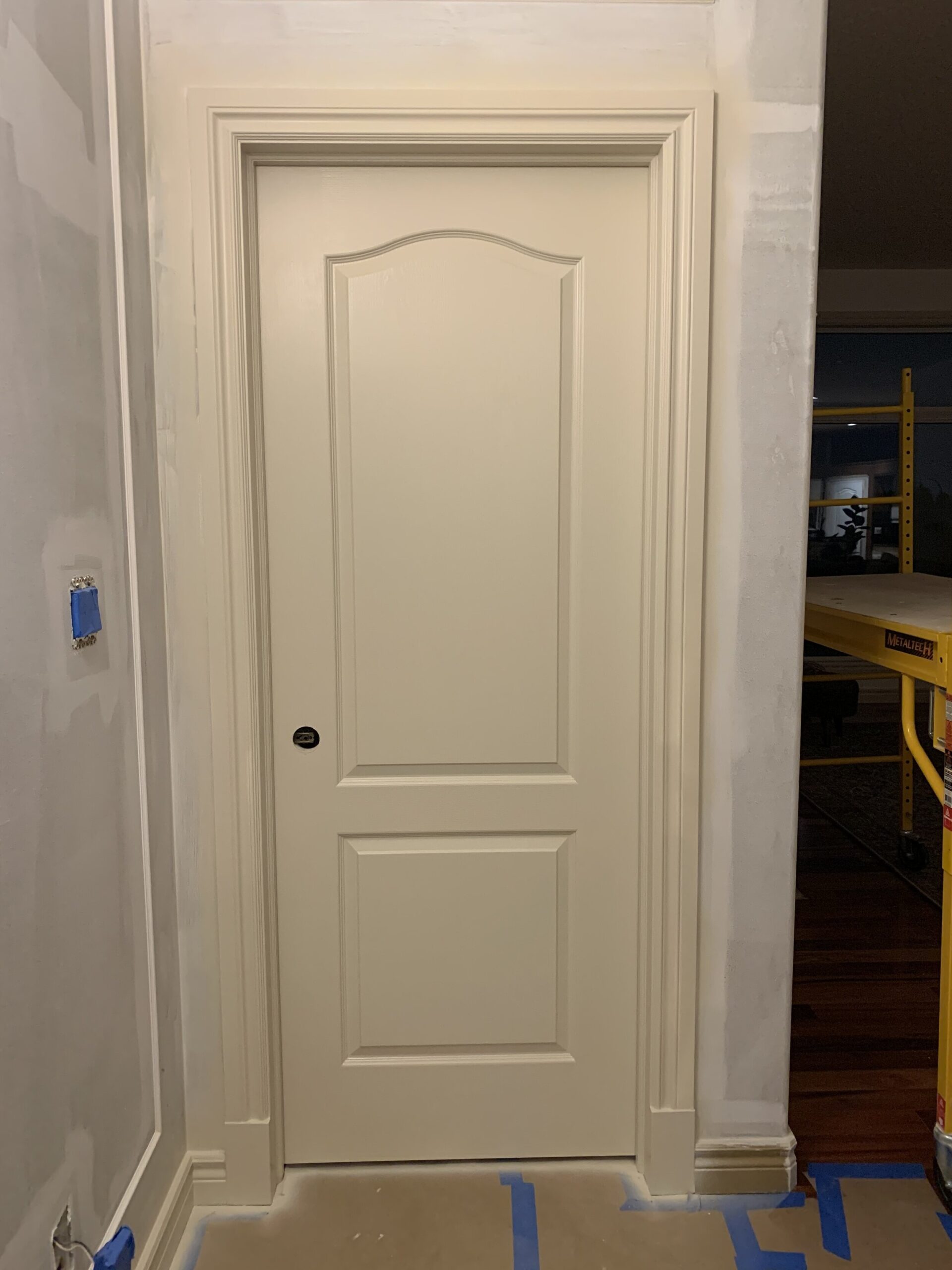 Door with new beige trim and new beige paint, walls with one coat of white paint