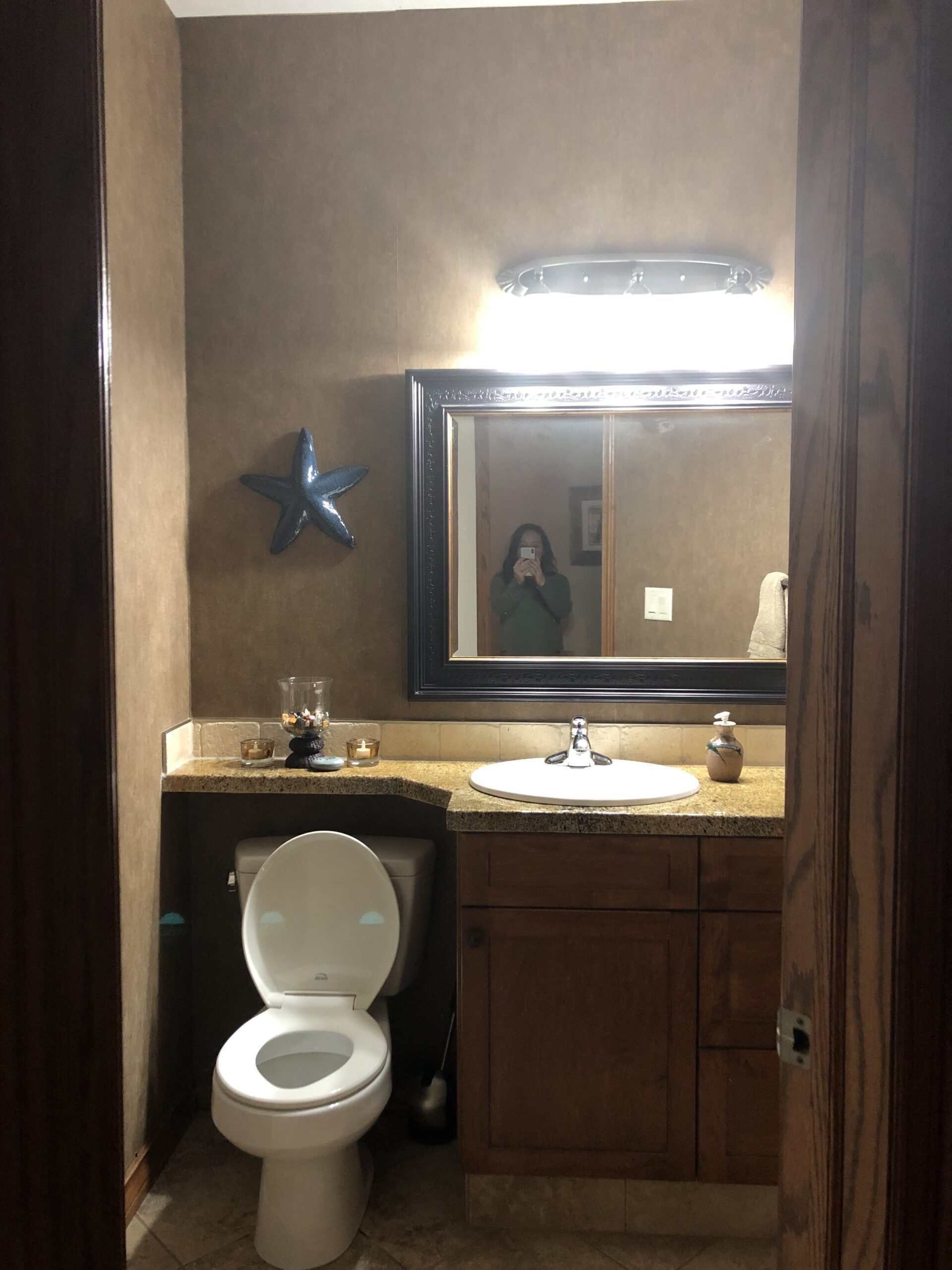 Before image of a bathroom with brown wallpaper, brown speckled granite, brown wood vanity