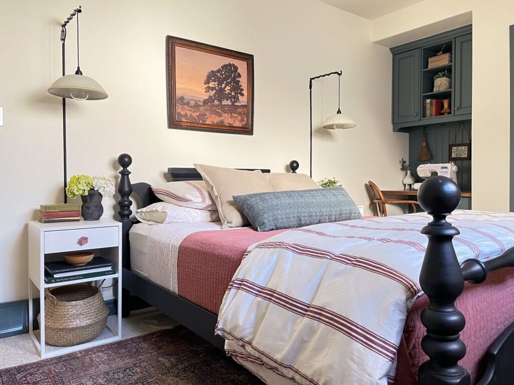 Bedroom with black painted antique bed, modern nightstands, ceramic wall pendants, striped pink bedding and contrasting blue grey trim and built in cabinets.