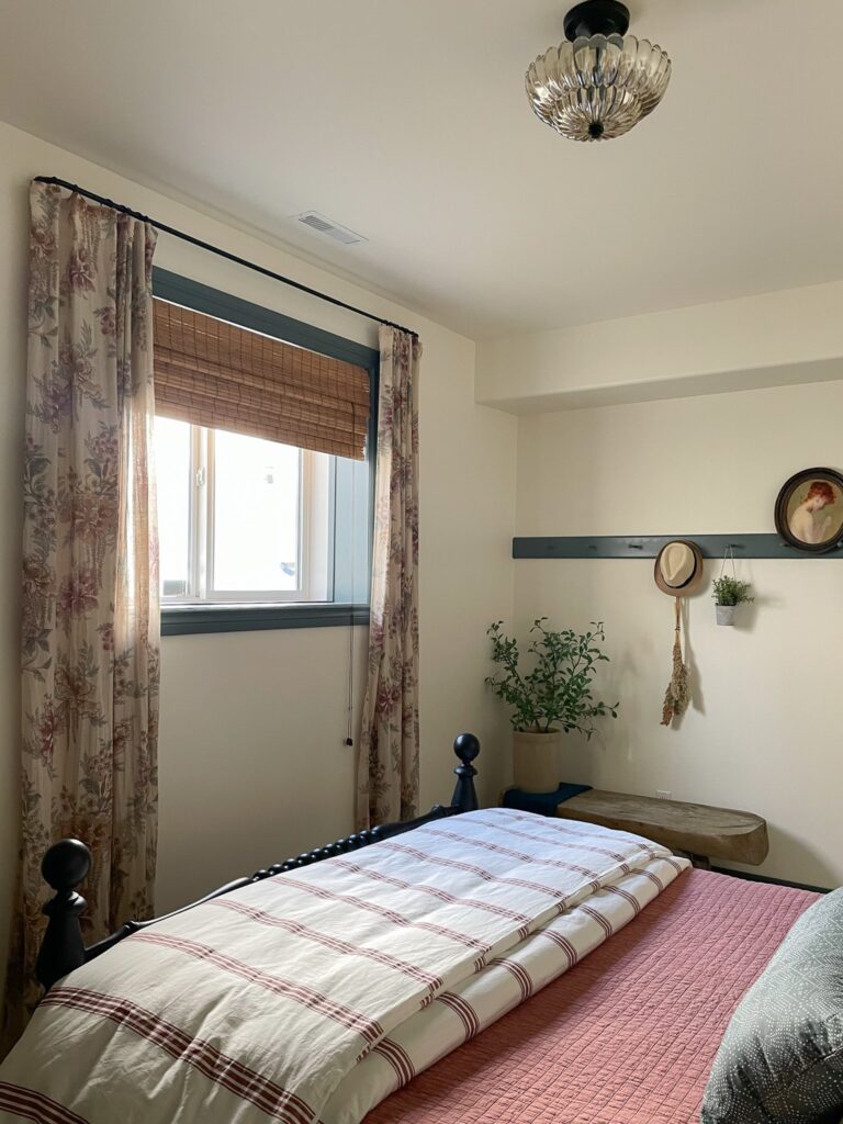 bedroom showing a smooth white ceiling and walls, window with floral curtains and woven shades, striped pink bedding, white walls and green contrasting trim and peg rail 