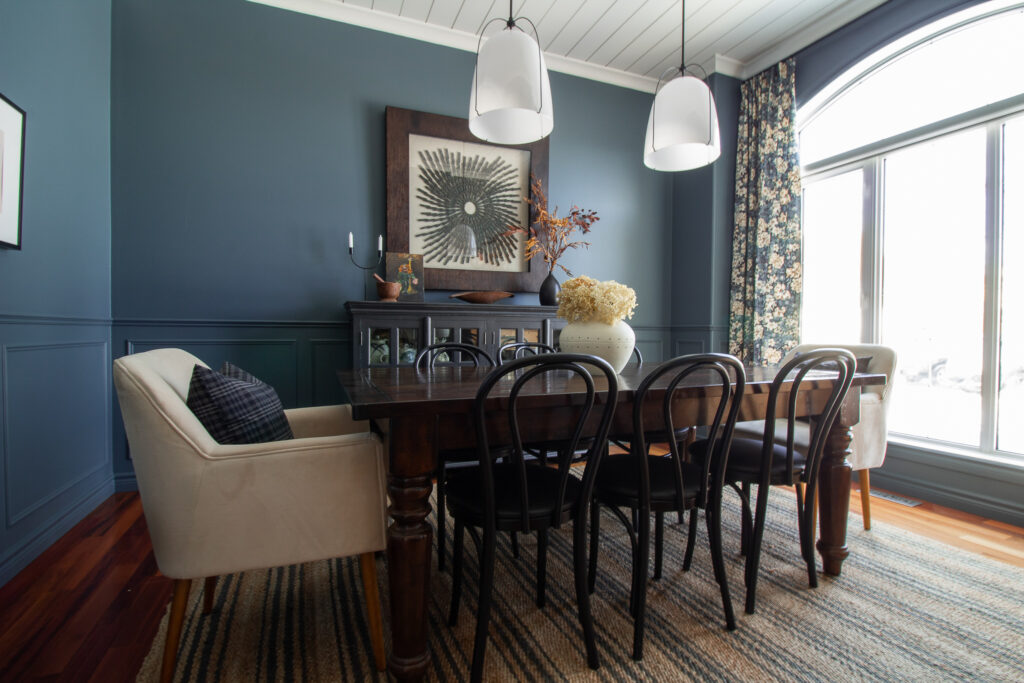 Blue dining room with chair rail, shiplap ceiling, floral curtains, striped jute rug and modern lighting.