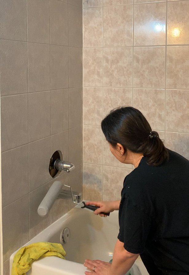 woman rolling primer on shower tile to prep to tile over tile