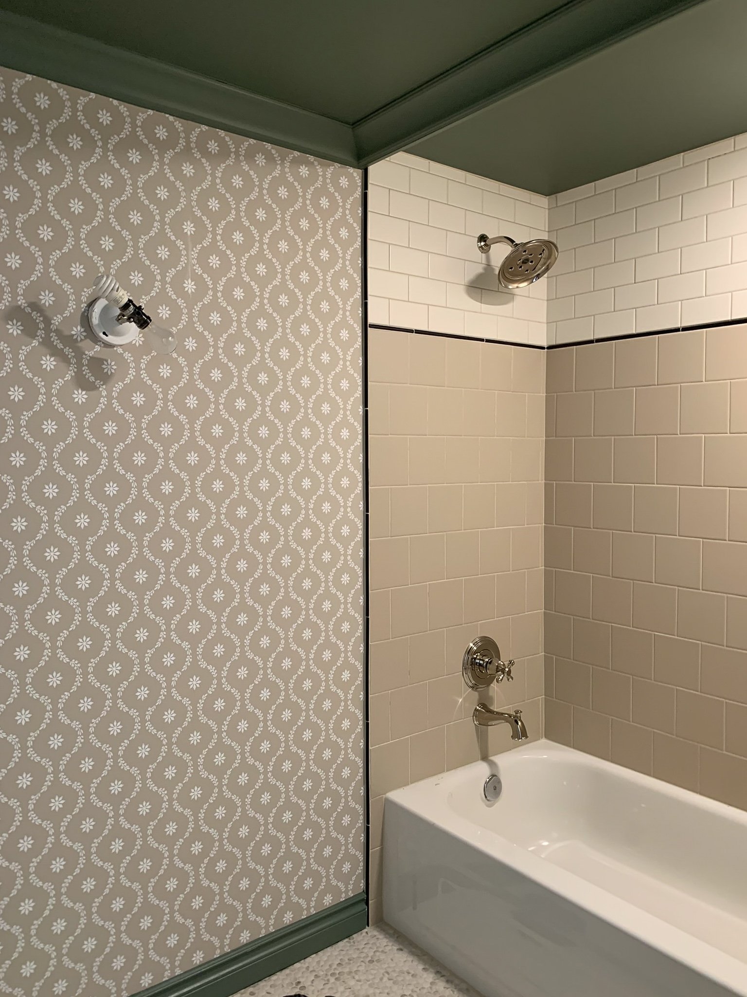 bathroom under construction with completed subway tile shower, new fixtures and cole and sons clandon trellis floral wallpaer and green ceiling 