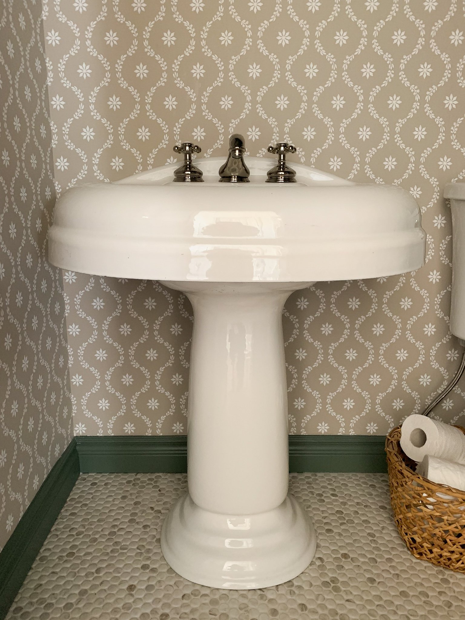 Vintage pedestal sinkw tih polished nickel fixtures and floral wallpaper, green trim and penny tile 