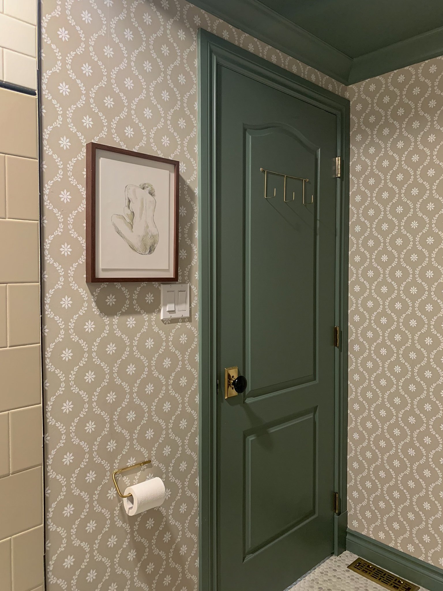 Green painted door with brass and black doorknob, with beige floral wallpaper