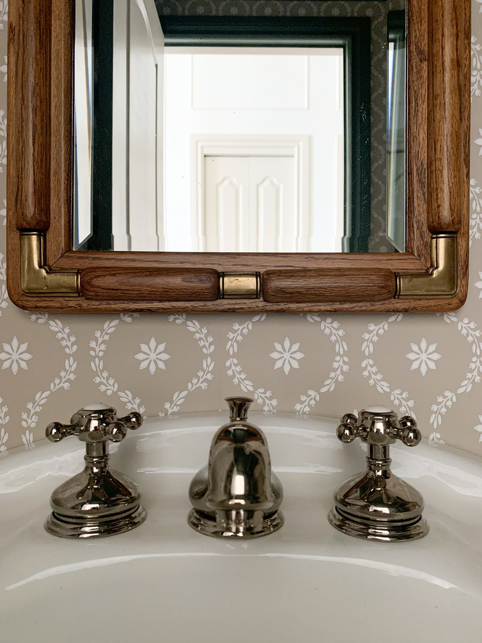 vintage wood and brass mirror over a pedestal sink with polished nickel fixtures