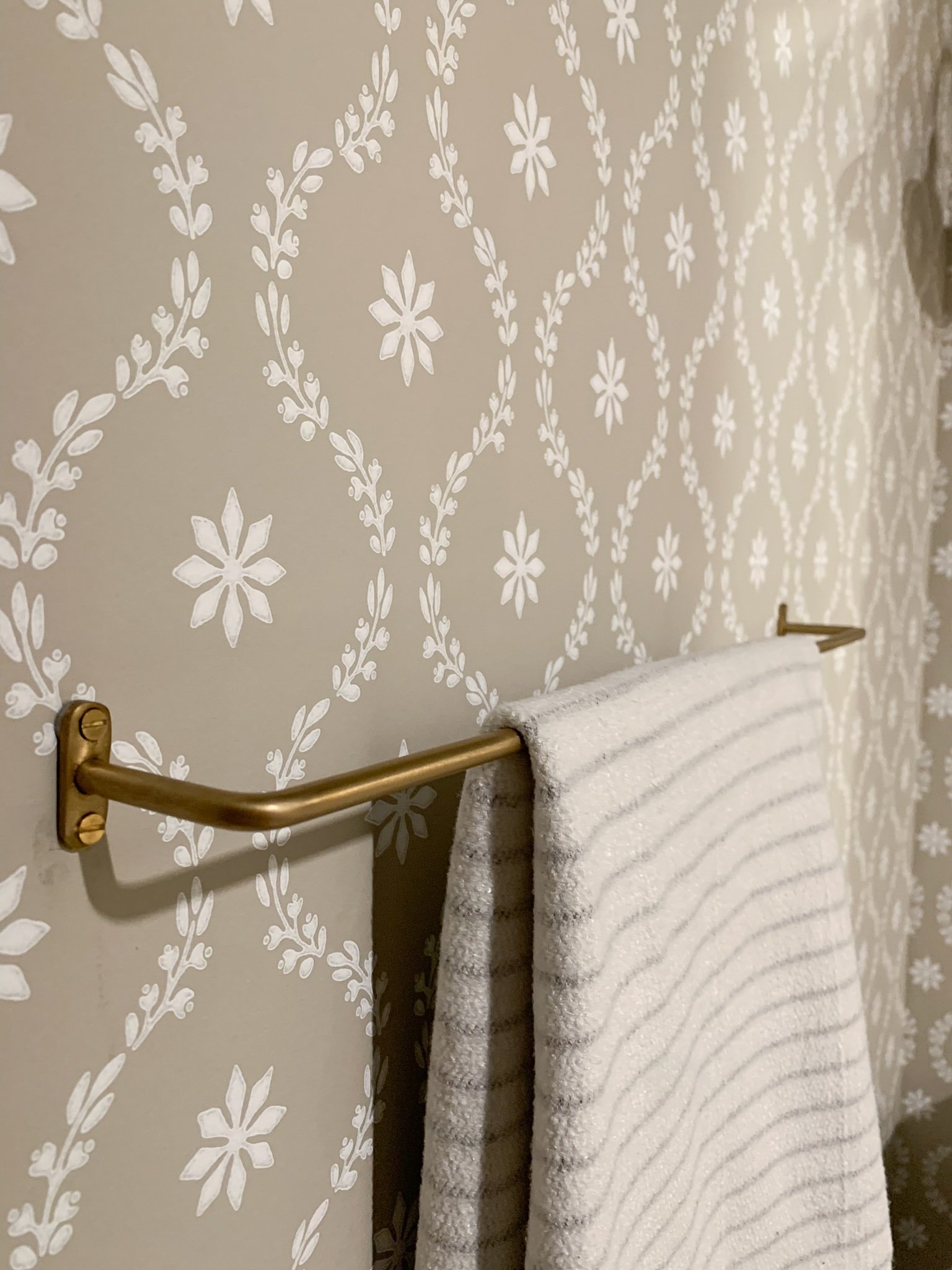 Modern brass towel bar with striped turkish towel on a floral wallpaper background