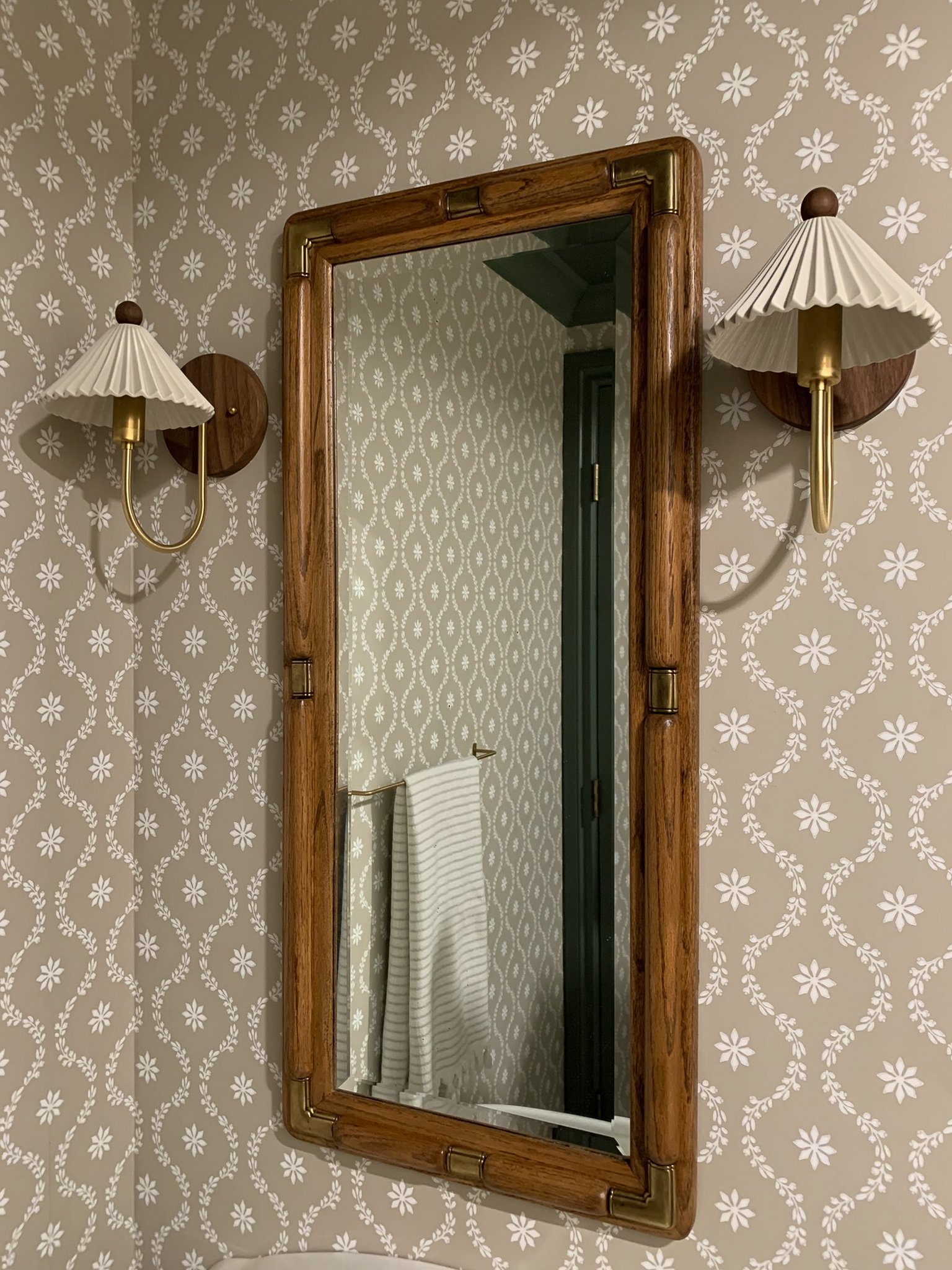 vintage wood and brass mirror on floral white and beige wallpaper flanked by huey light shop wood brass and ceramic sconces