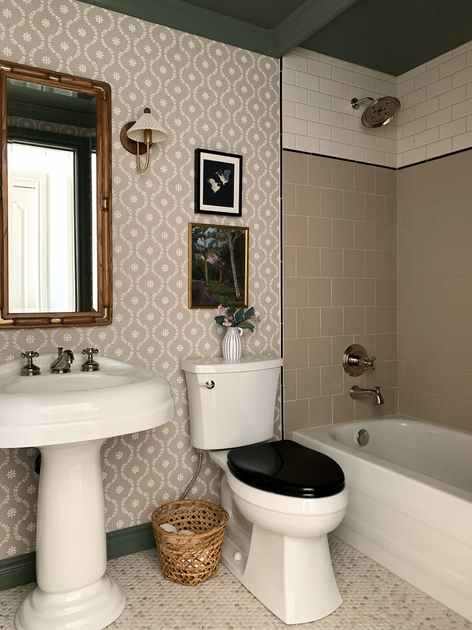 Bathroom with subway tile shower pattern, green ceiling, floral wallpaper, vintage sink, vintage mirror, brass sconces, black toilet seat, penny tile floor