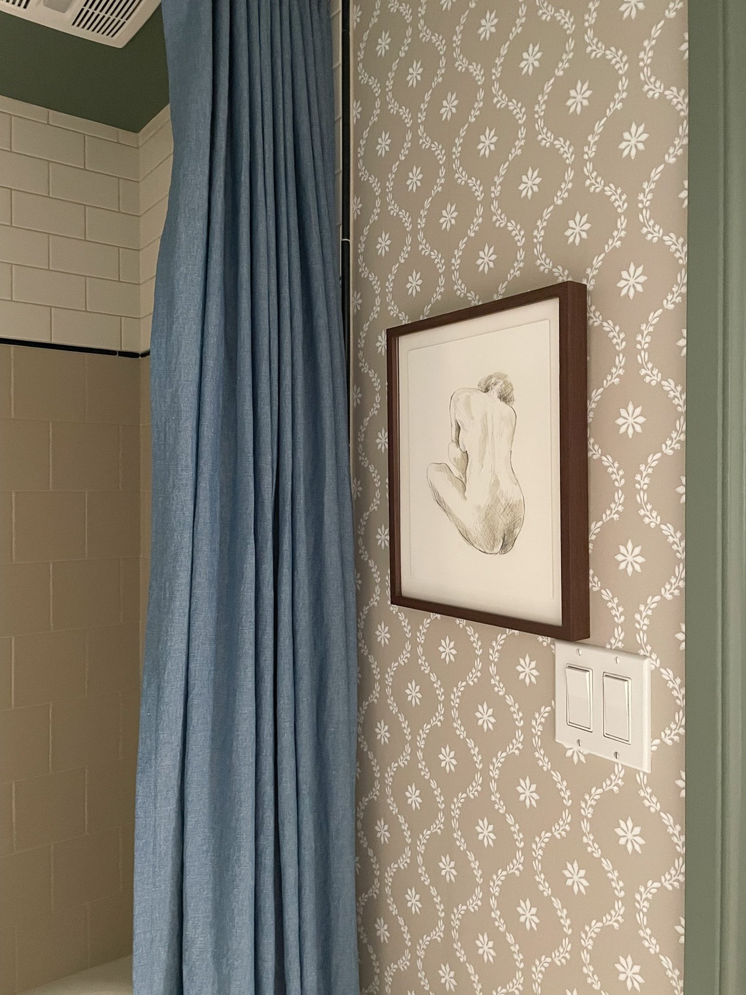 art with sketch of woman in a walnut frame, with blue linen shower curtain and subway tile shower in background, on a wallpapered wall