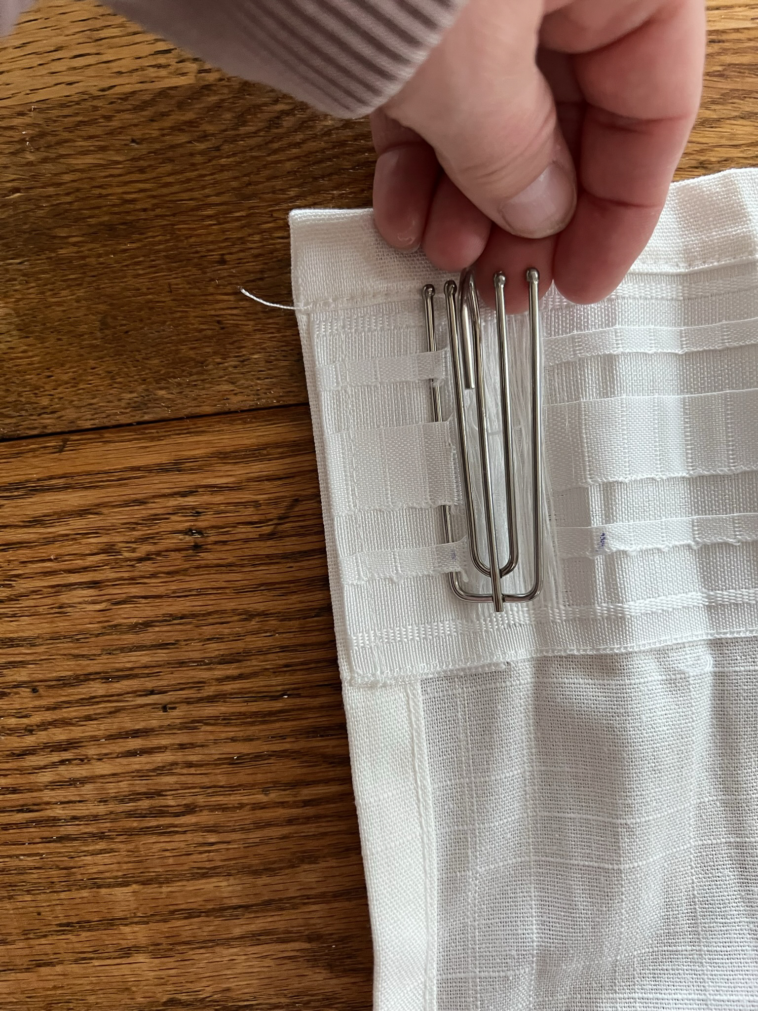 First prong of triple pinch pleat curtain hooks inserted into the curtain about 1" from the end of the curtain on the header tape