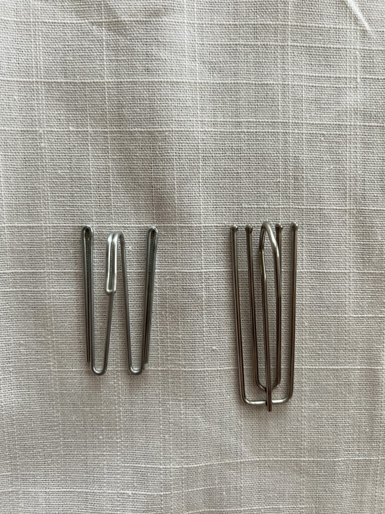 a two prong and a four prong curtain hook side by side on a white background