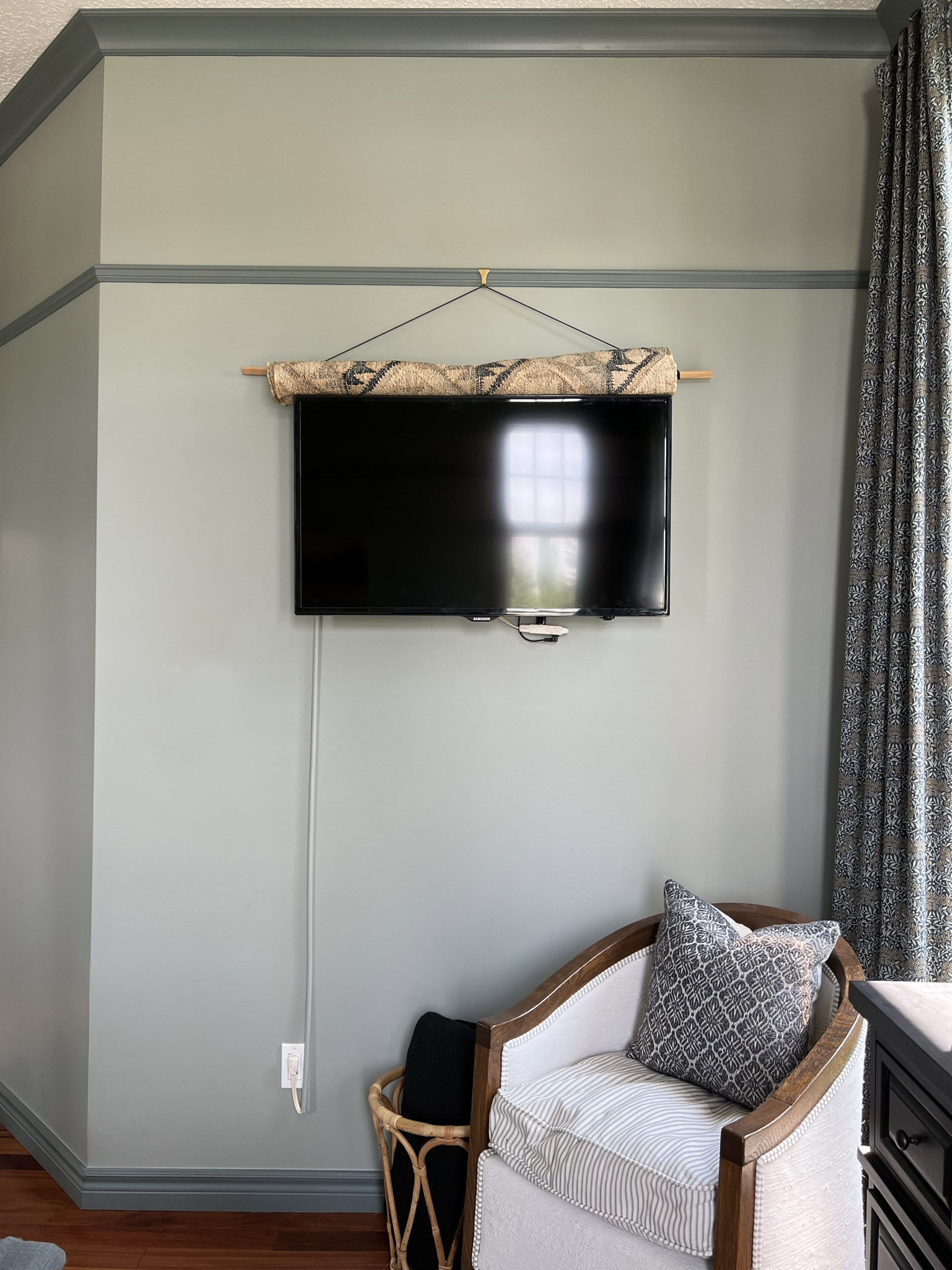 Rug  rolled up and sitting on top of a tv in a room with green walls and dark green contrast trim.  Antique chair in foreground