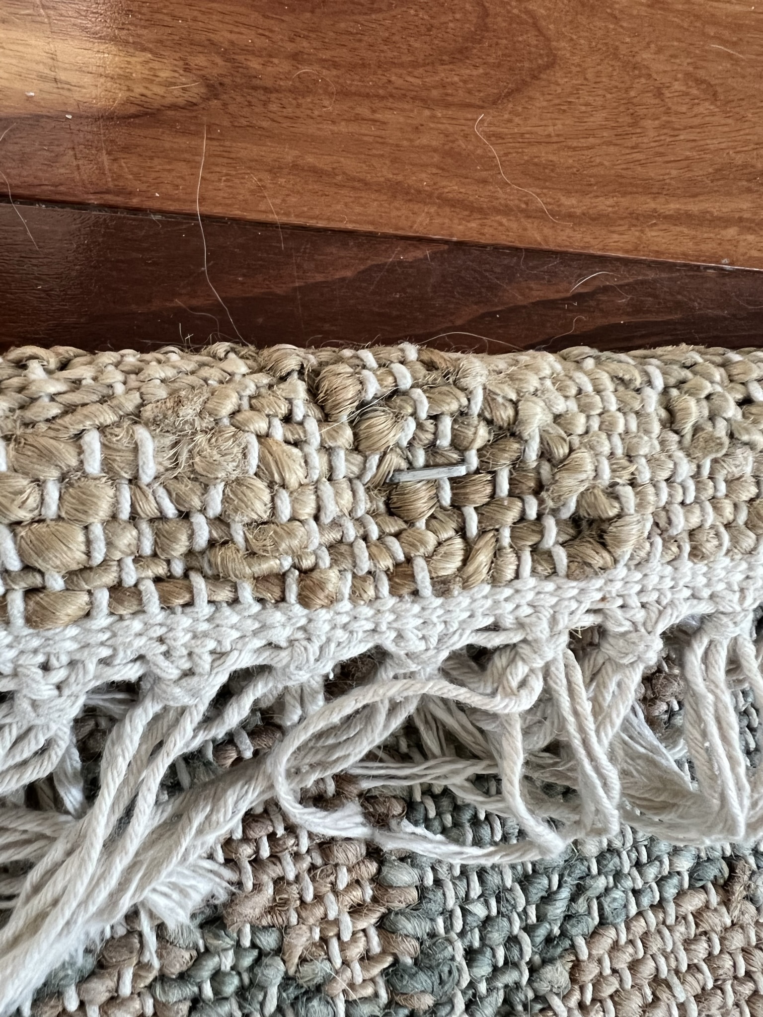 Close up of a rug folded over a piece of wood with a staple in it to hold in place