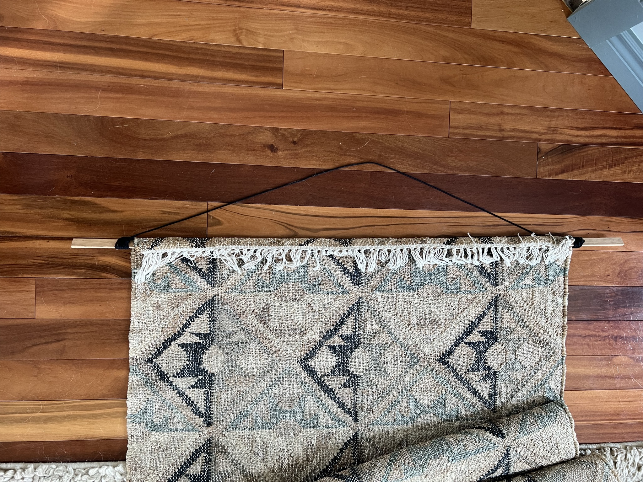 To hang a rug over a TV, the Top of a rug is folded over a wood piece with string tied to either end.