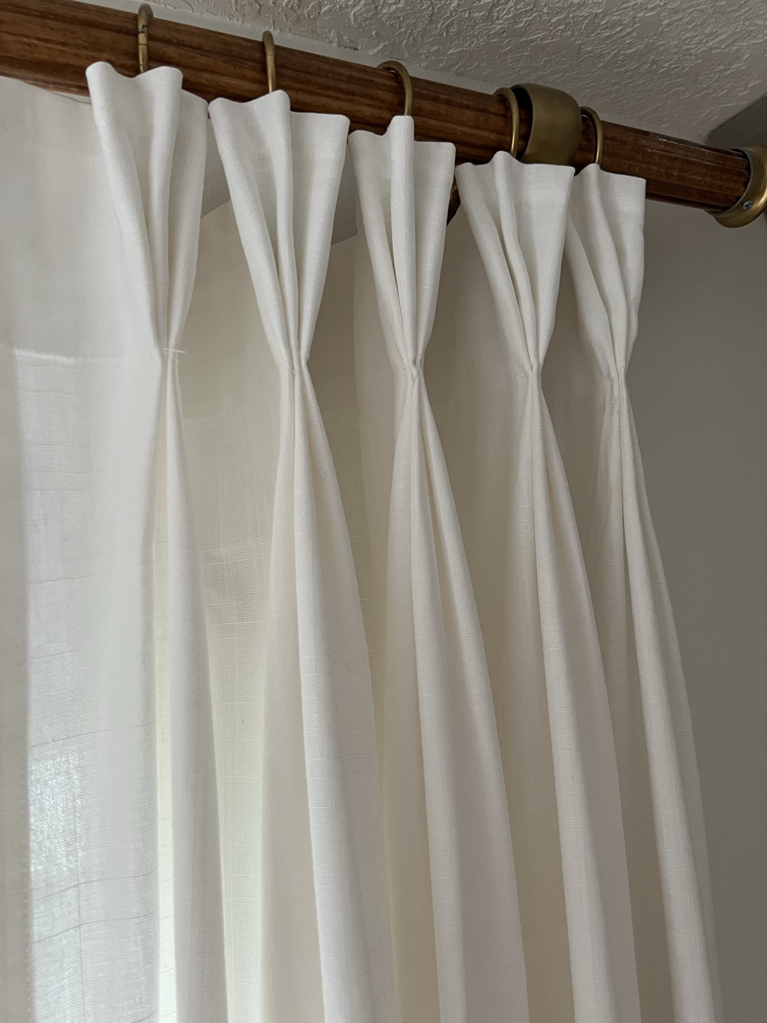 Close up of DIY Pinch pleat curtains near the top of the curtains showing the pleats and how they are hung on a wood and brass curtain rod