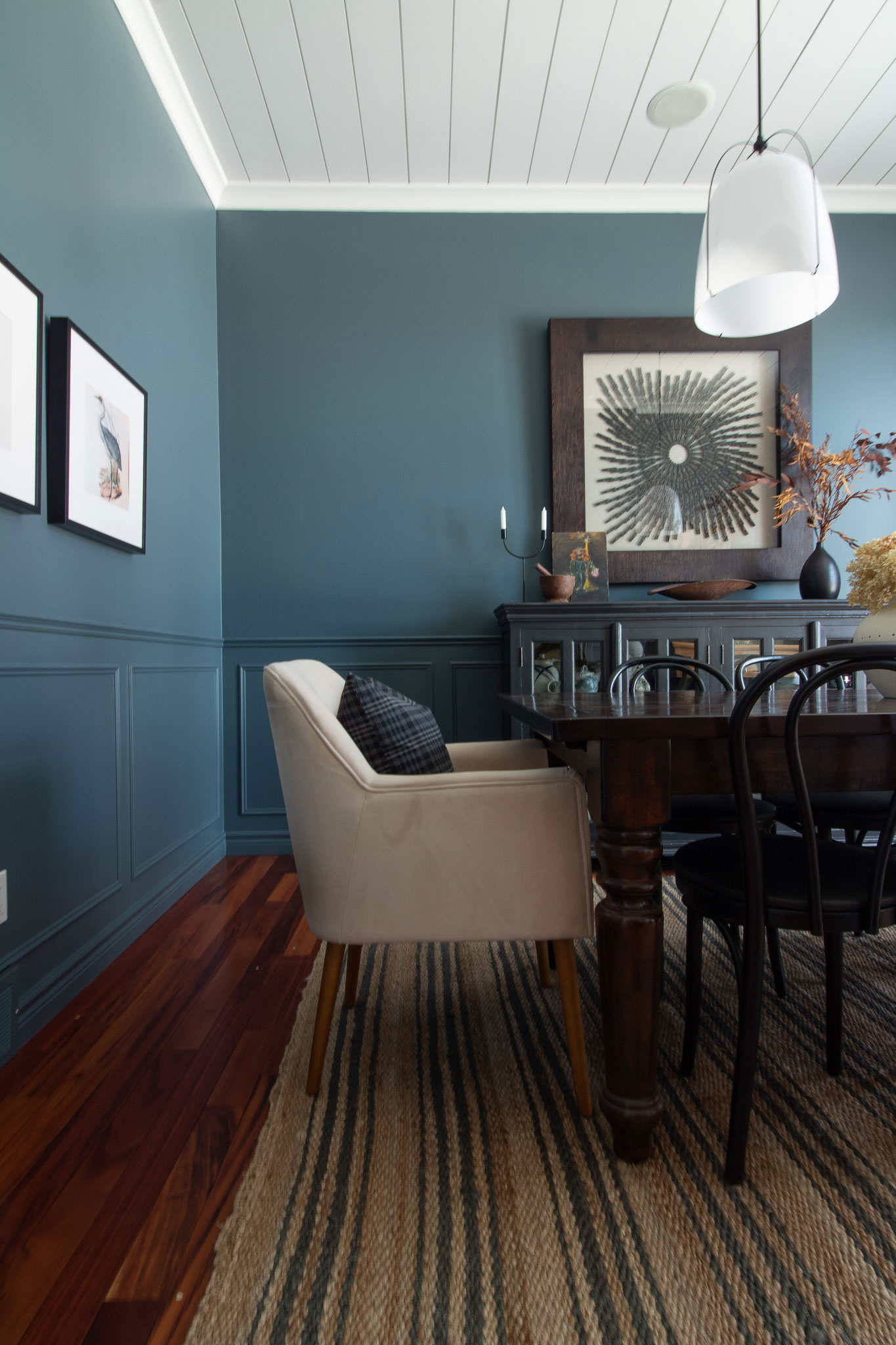 Dining room with jute rug with stripes, wood table, black bentwood chairs, white end chairs, blue walls, rejuvenation pendants, large art 