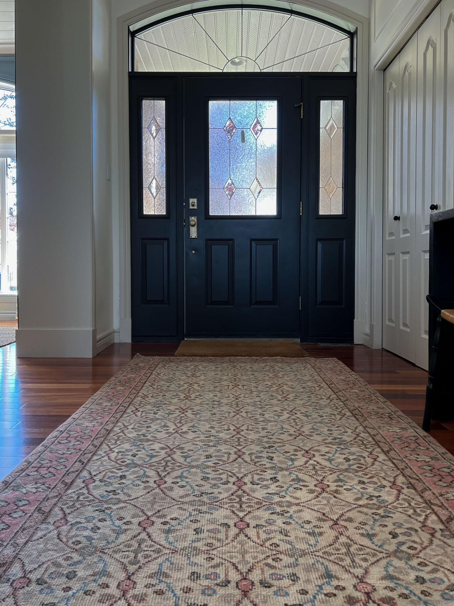 entry showing a black door with sidelights, white walls and beige contrast trim, and a red and blue large sized vintage rug