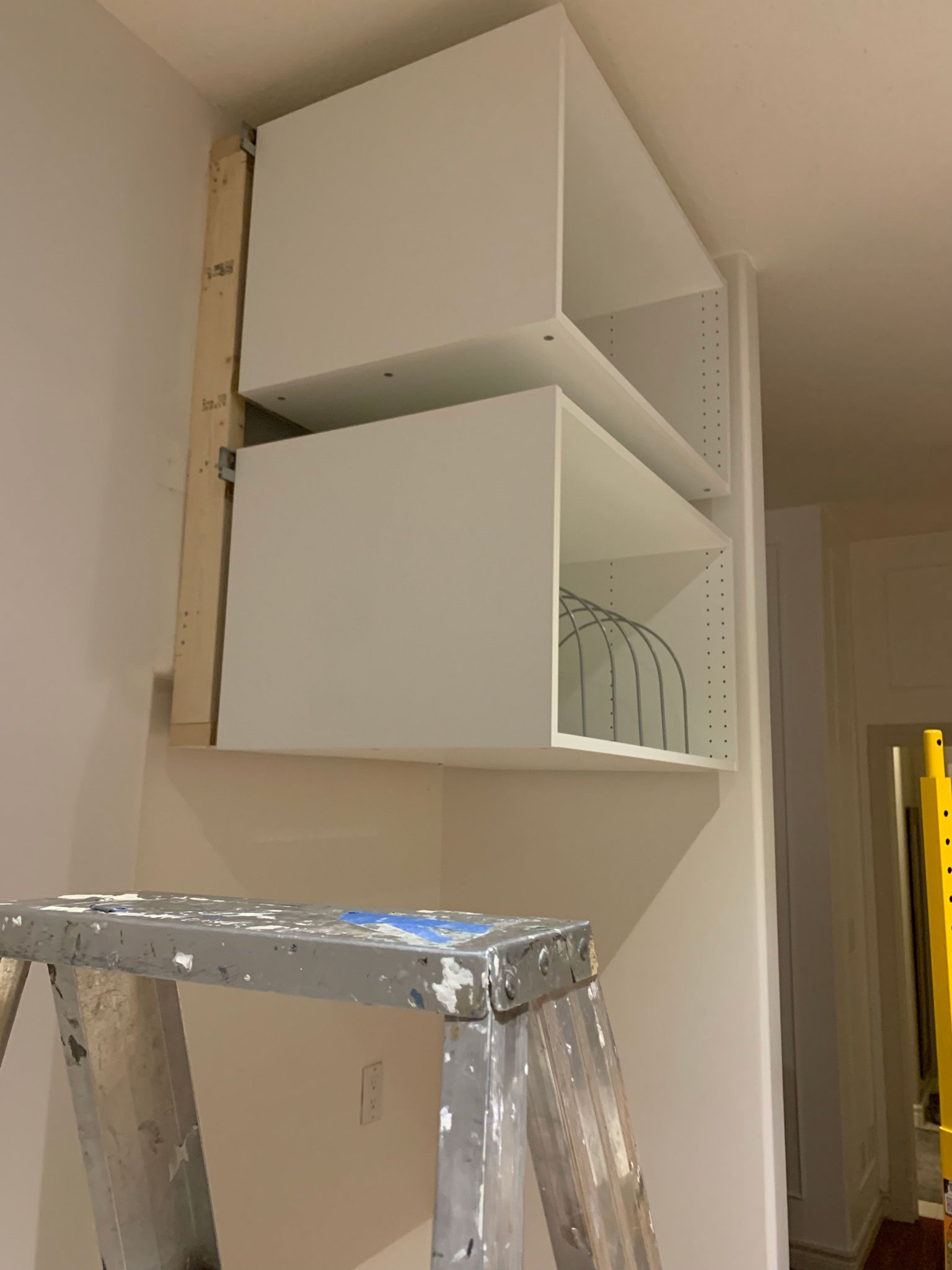Two cabinet boxes hanging on the wall, view from the side showing framing set behind in order to make refridgerator look more built in
