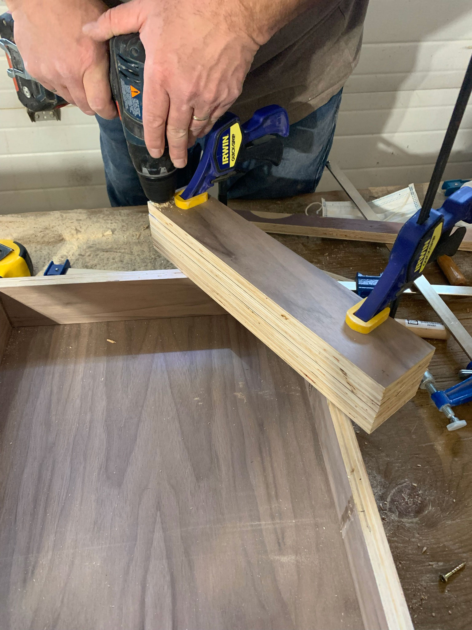 Shelves clamped together and man drilling hole through all the shelves at once.