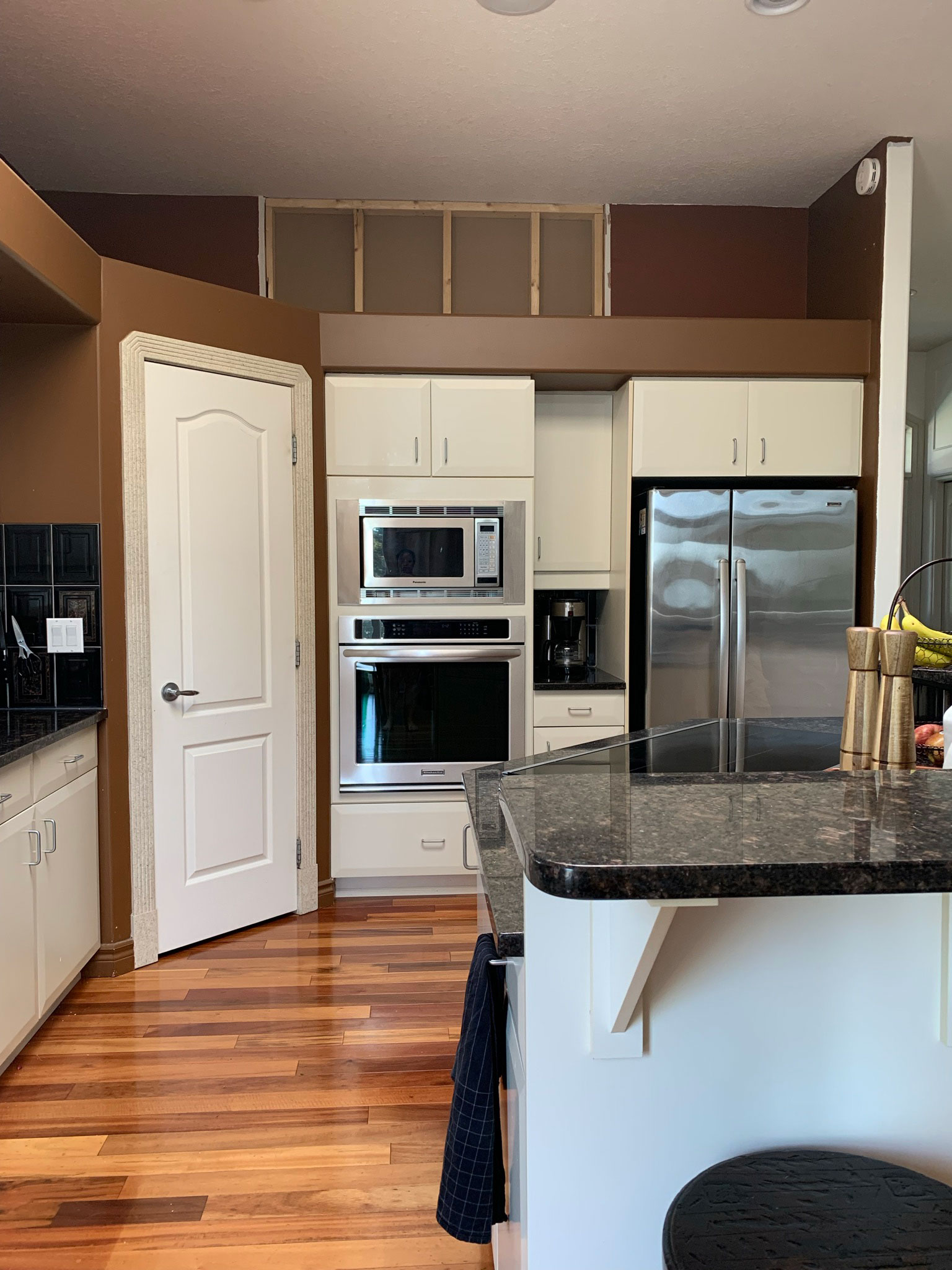 before photo of kitchen with white cabinets, built in oven and microwave, corner pantry, fridge with space around it and a bulkhead over cabinets