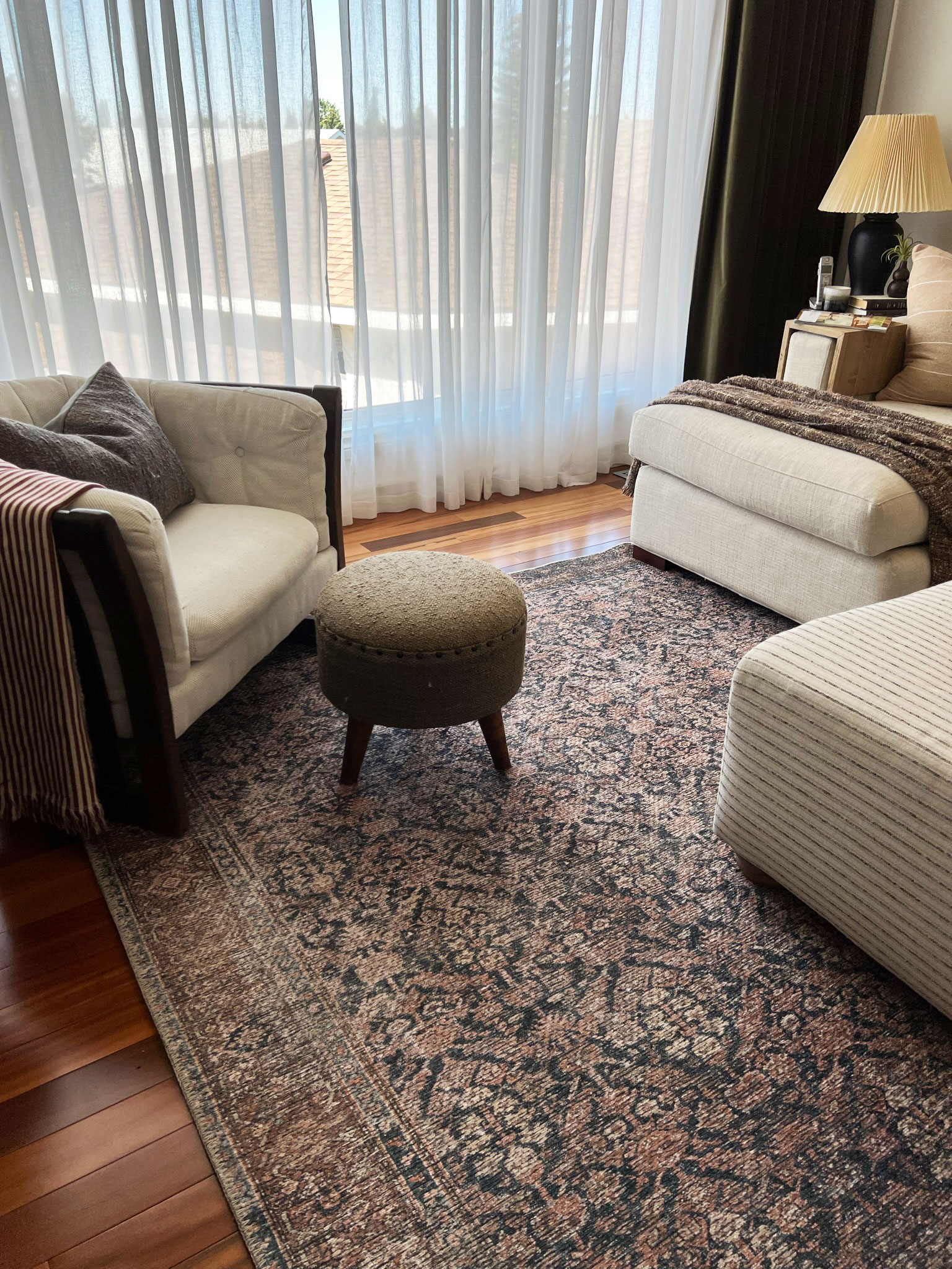 living room showing all front legs of furniture on the rug, with a vintage look blue and pink rug, white furntiure and a stool with a large window