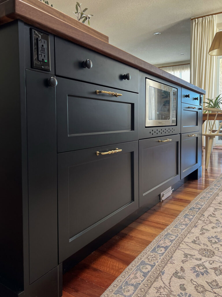 Black island with wood top and wood floors, brass hardware, all drawers with skinny cabinets at either end, made by customizing the width of an ikea cabinet