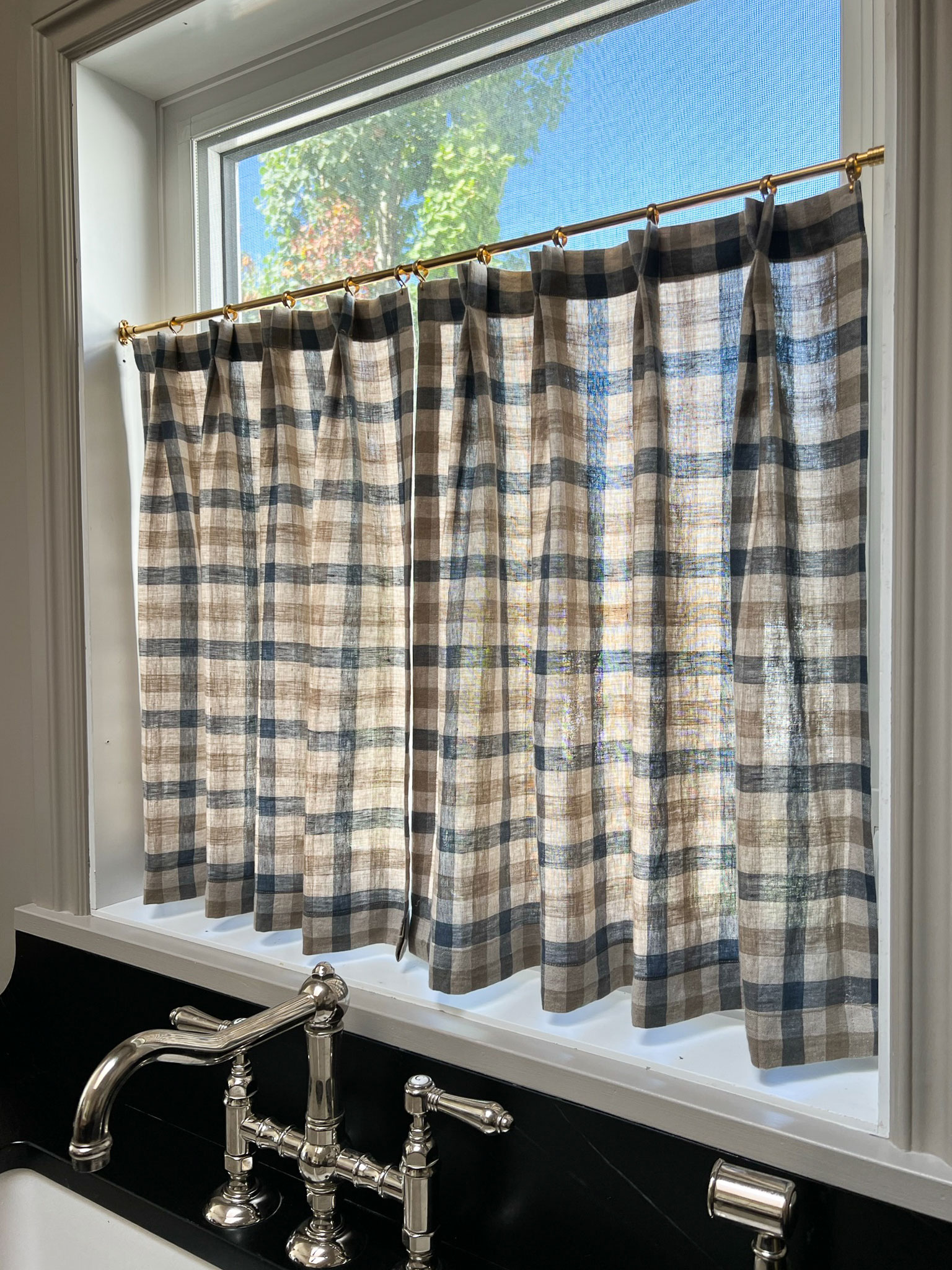 blue and beige checkered gingham lined cafe curtains with double pleat in kitchen window with polished nickel faucet below