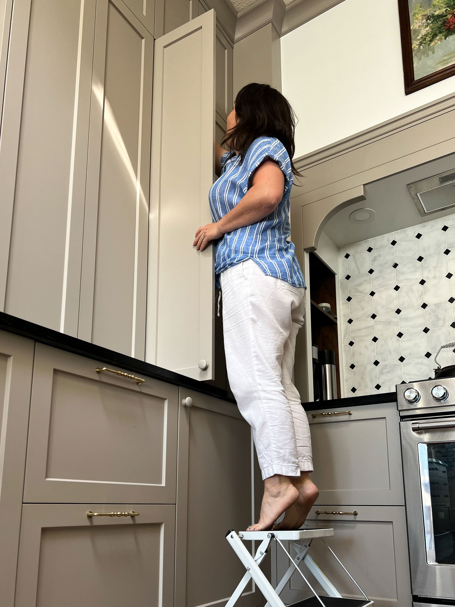 Woman using a stool to reach high cabinets