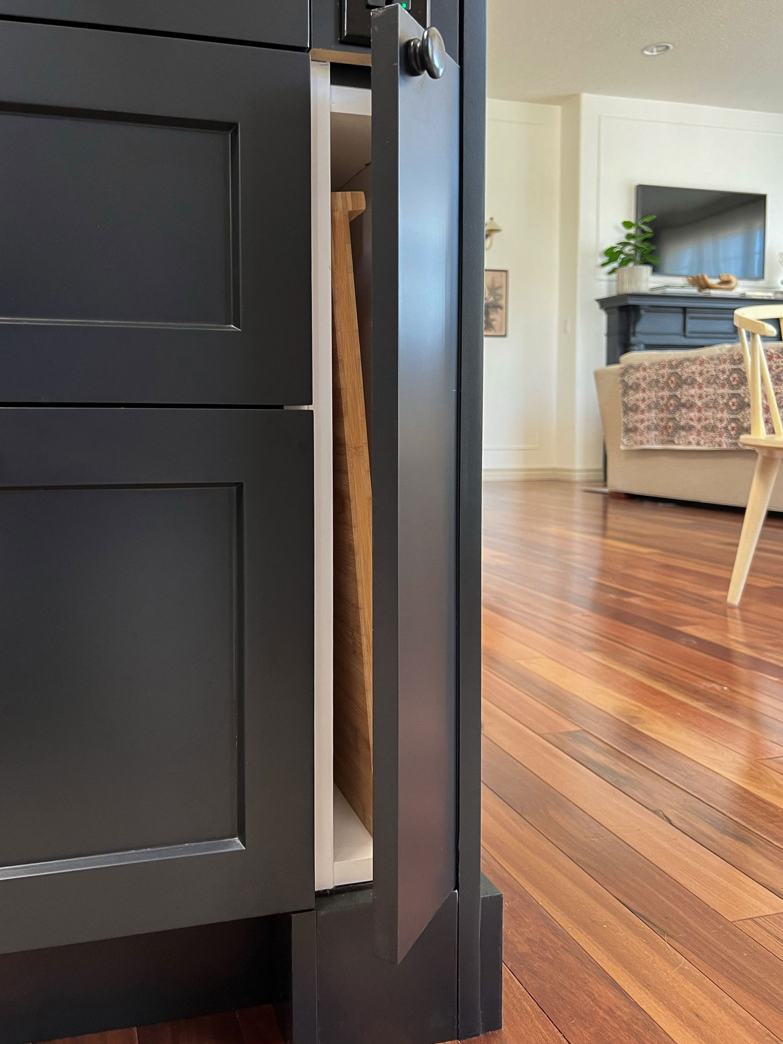 A skinny 4 1/2" ikea cabinet opening showing a cutting board inside, in a black island cabinets