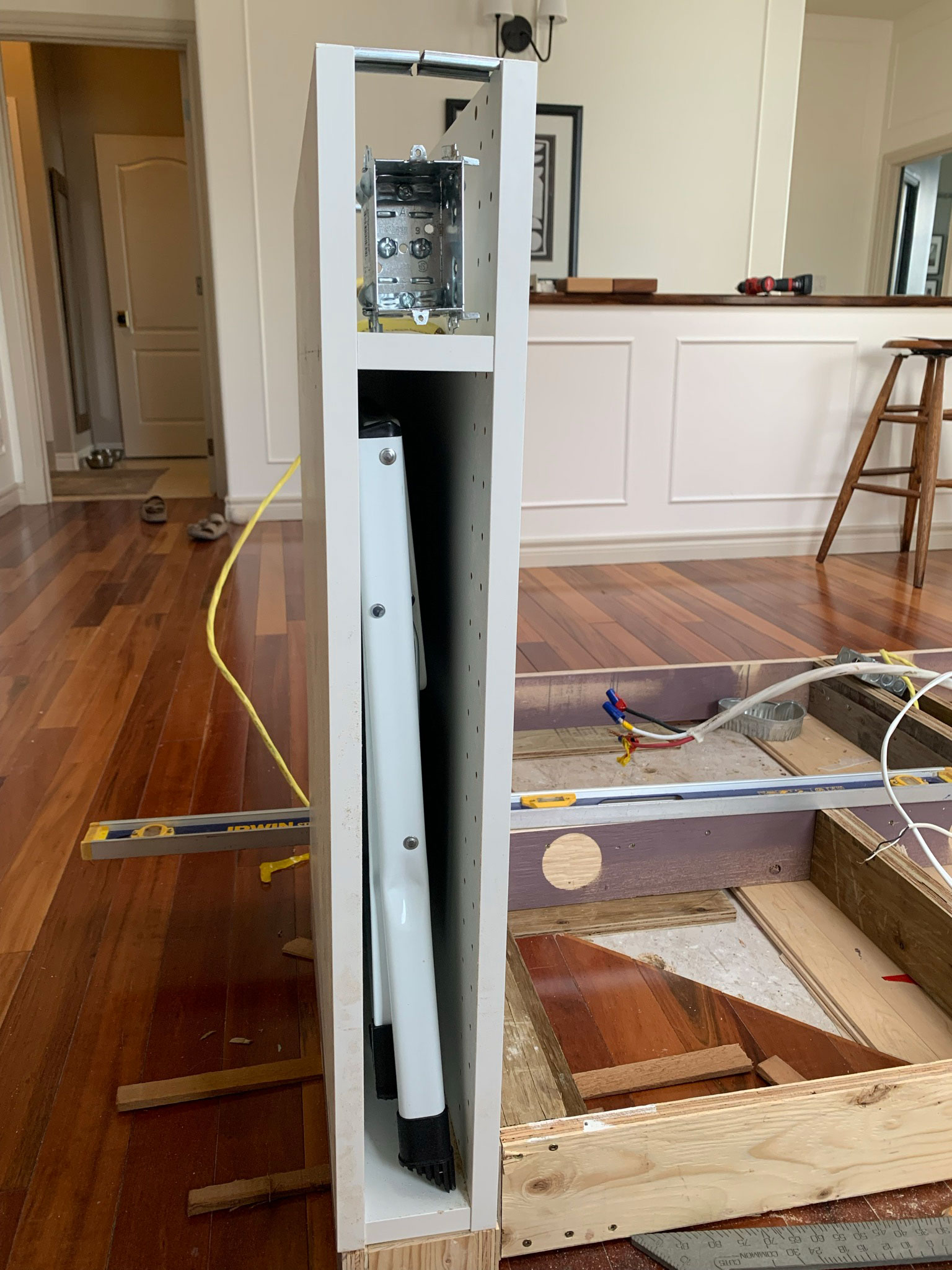 Skinny cabinet with stool inside and an electrical box on the top, with a shelf separating those two areas.