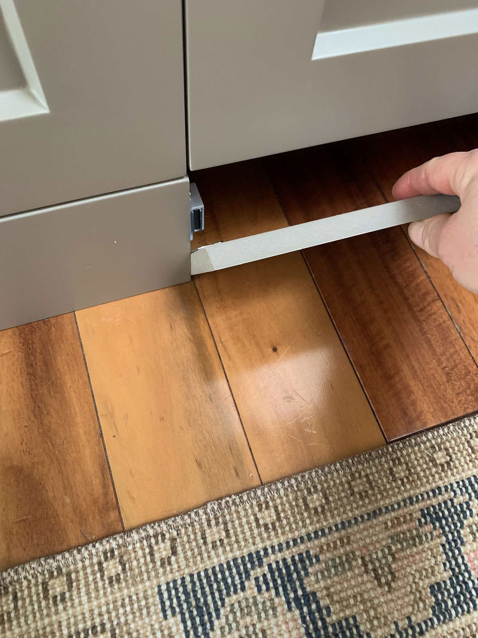 Removing a toe kick from infront of a dishwasher showing the magnets holding it in place