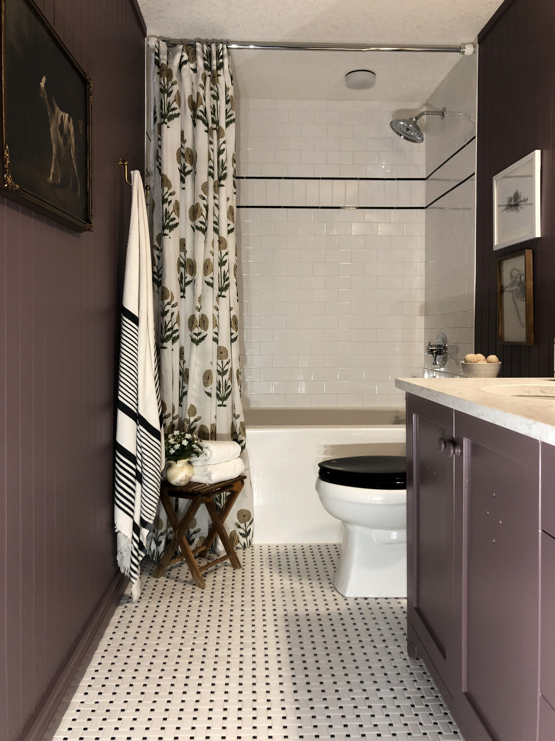 purple bathroom with basketweave tile floor, beadboard walls, block print curtain, white toilet with black seat, subway tile walls