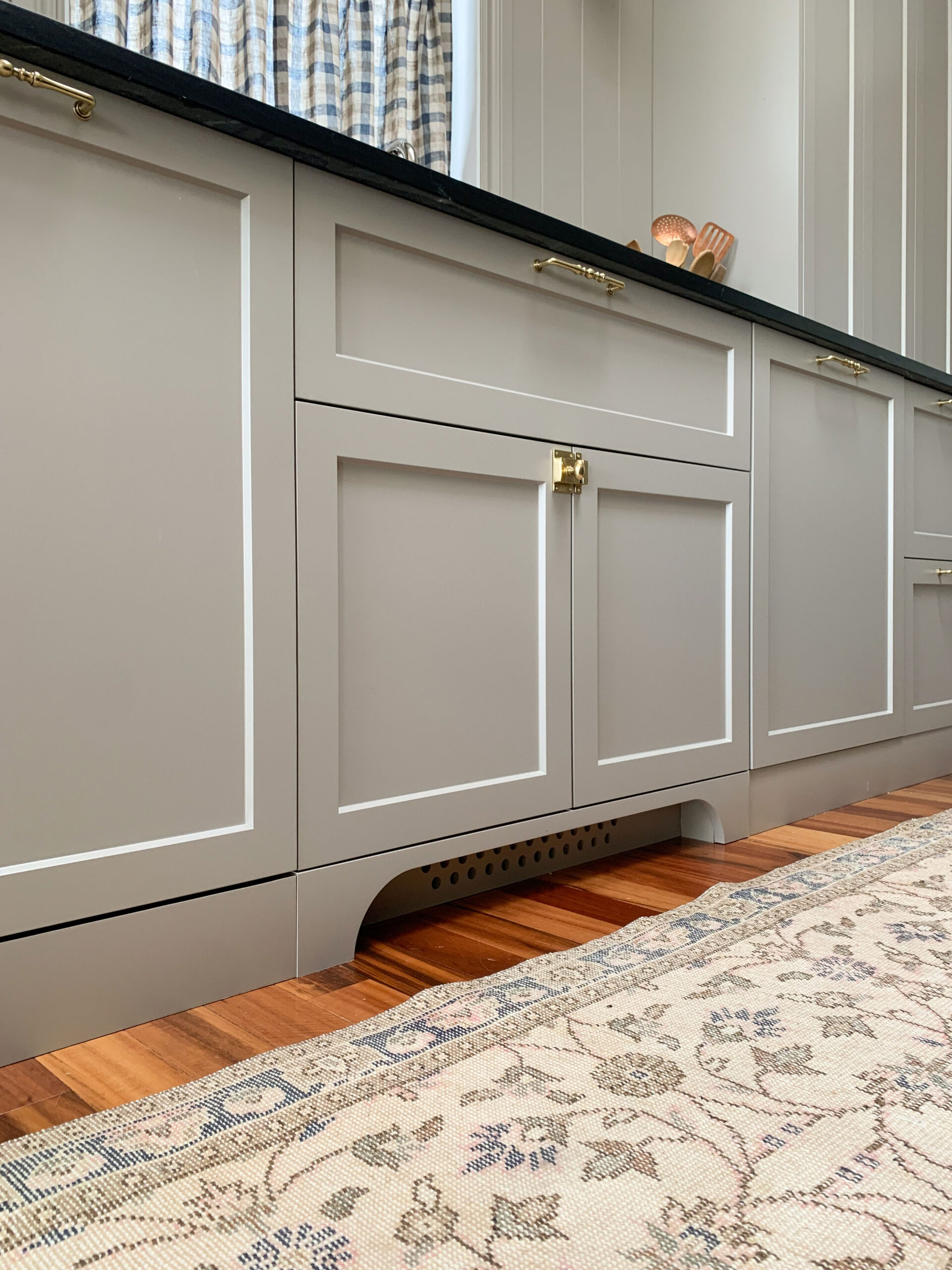 Cut out decorative toe kick, beige cabinets, black soapstone counters in front of a kitchen sink