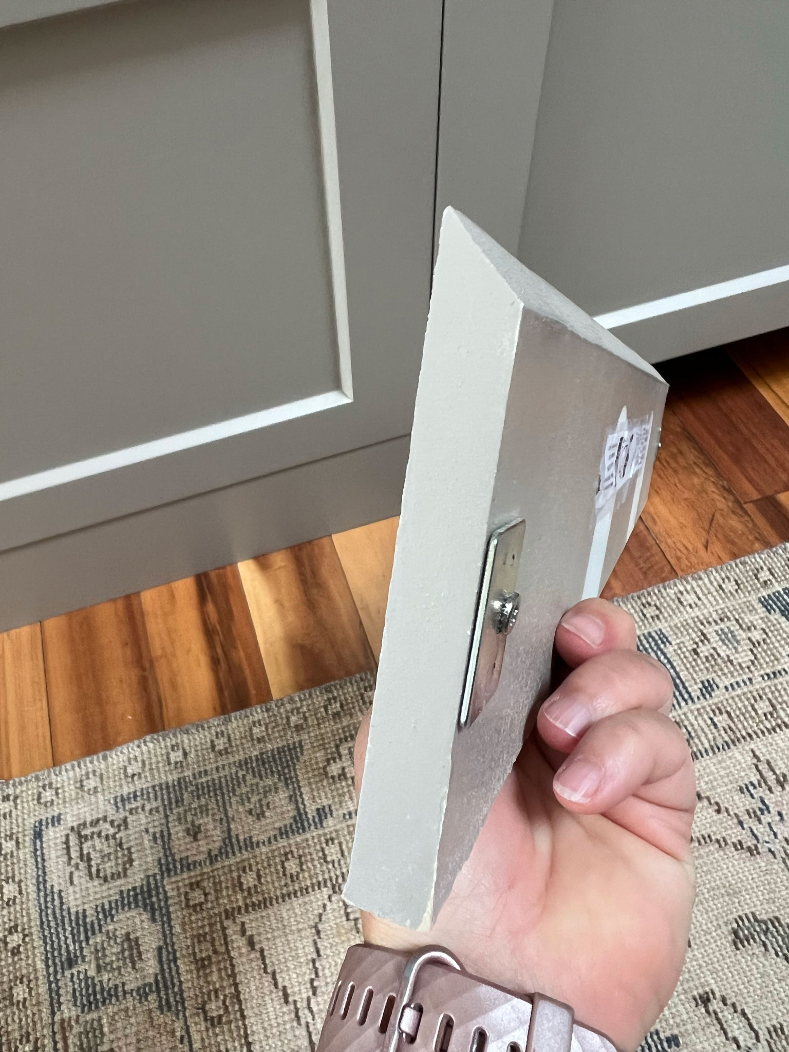 holding a piece of cabinet toe kick that was cut with an angle on the top and a metal plate attached to the back for a magnet