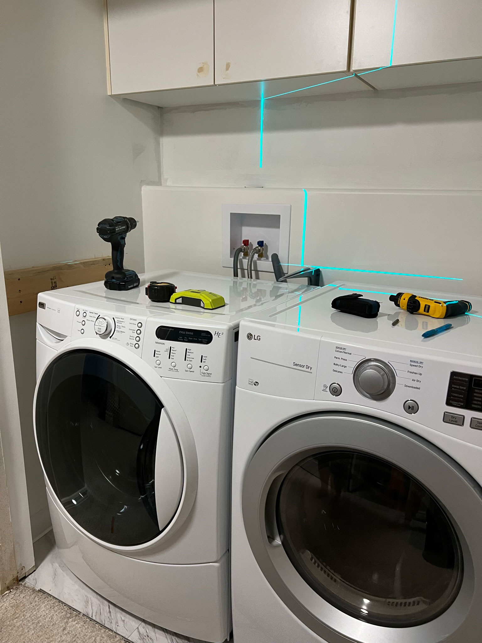 laundry cupboard with laundry machines and some tools and a laser line on top, a wood 2x6 screwed to the wall alongside