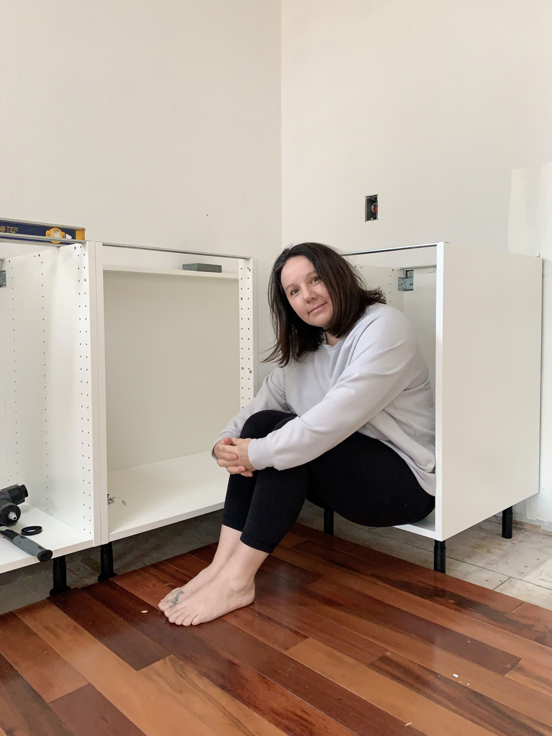 Ikea base cabinets installed with no doors showing the legs, woman sitting in cabinet