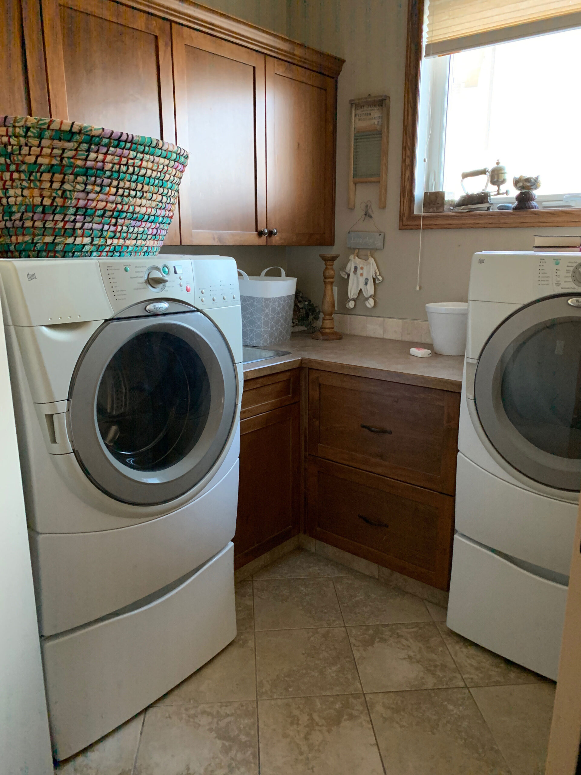 laundry room with wood cabinets, beige counters, beige tiles, beige walls, basket on wahser, window