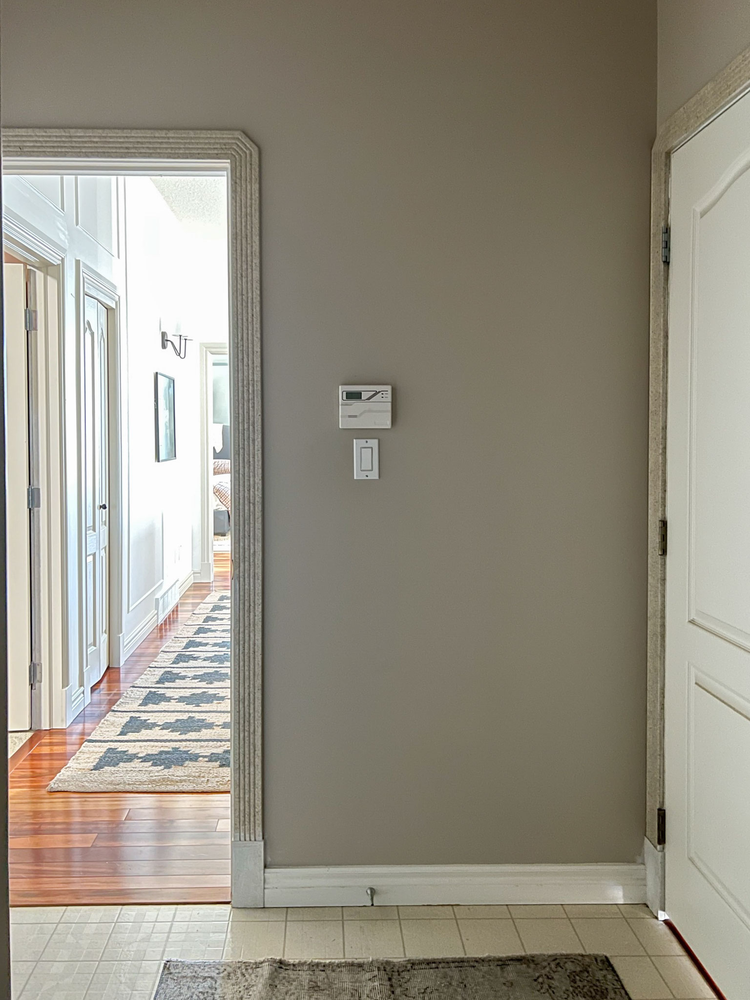 Mud room before looking with one door open on left looking down hallway, door closed on the right.  Beige walls, white trim, linoleum floors