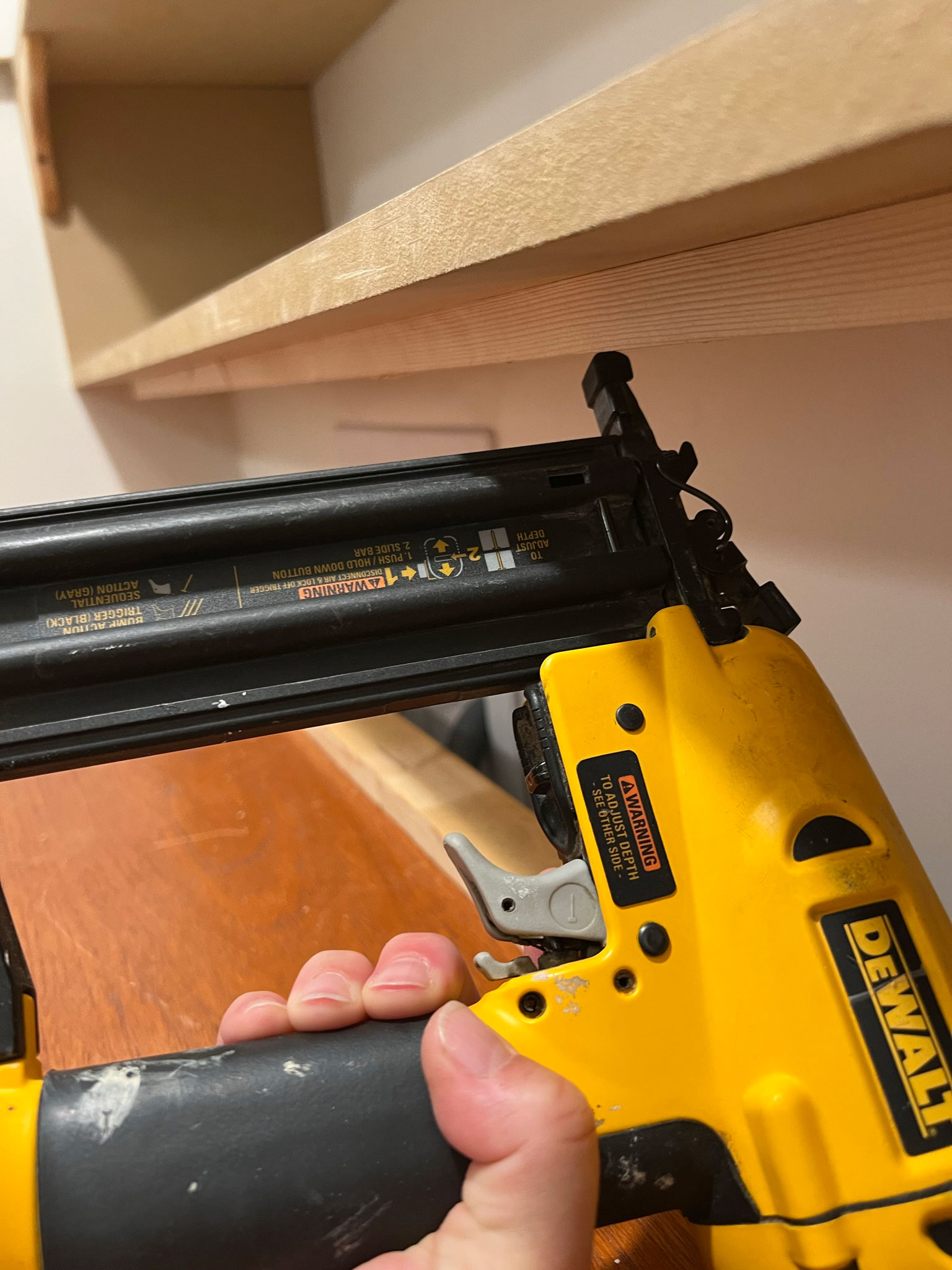nailing a piece of wood to the underside of a shelf using a nail gun