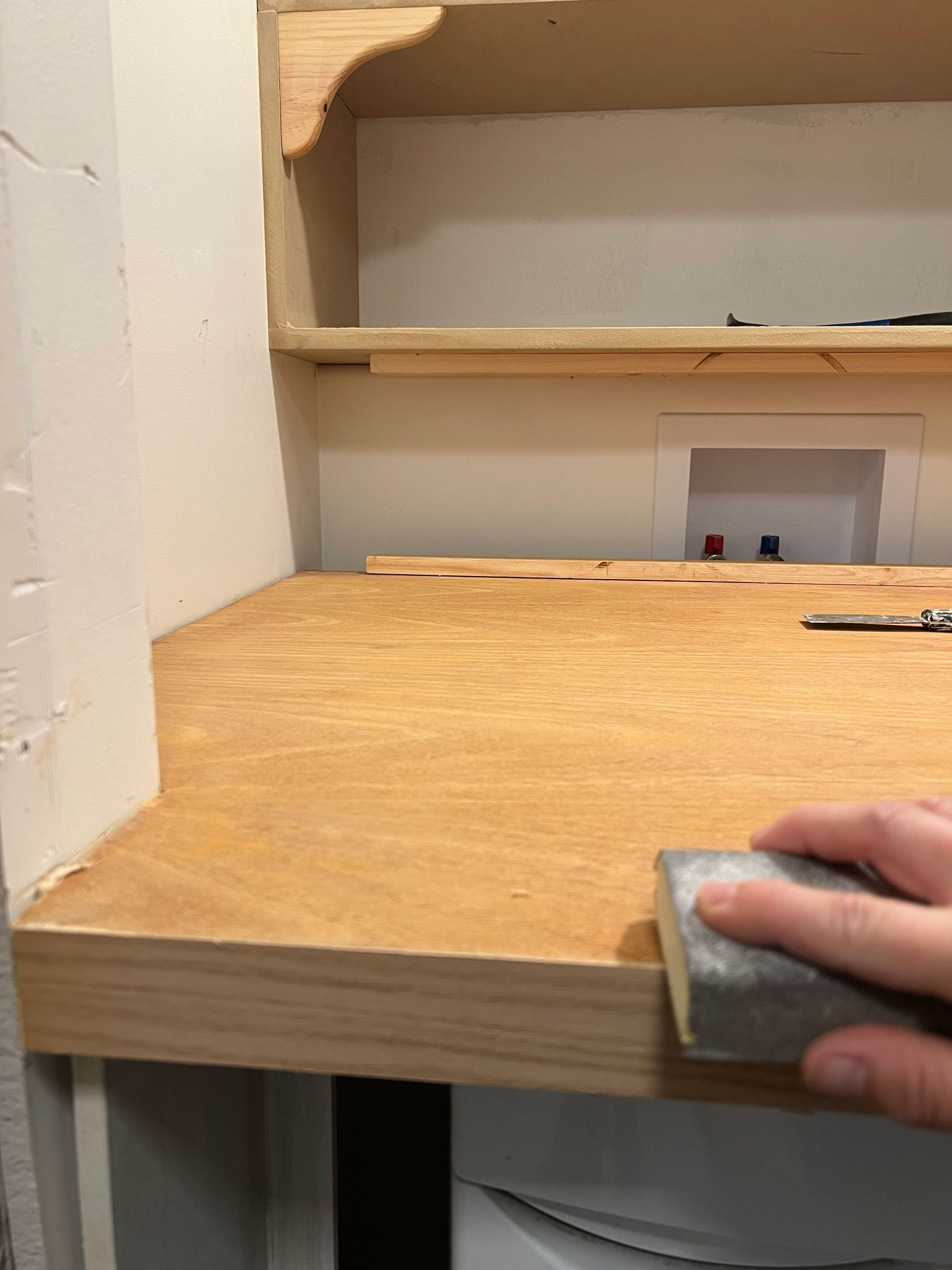 sanding the edge of veneer on the wood door we used to make the DIY laundry room countertop by hand with a sanding block