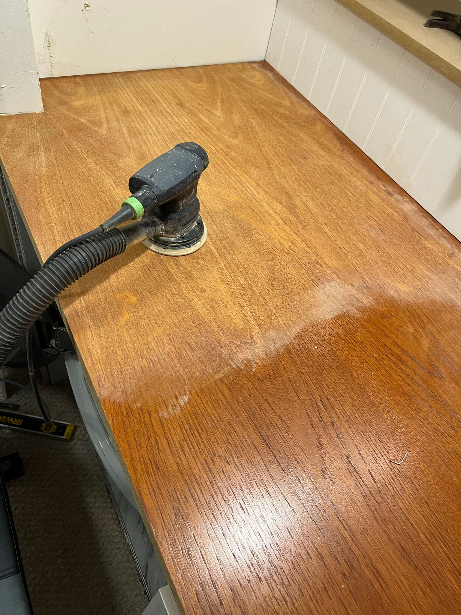 wood door in place for the DIY laundry room countertop, half sanded with a sander attached to a vacuum sitting on it